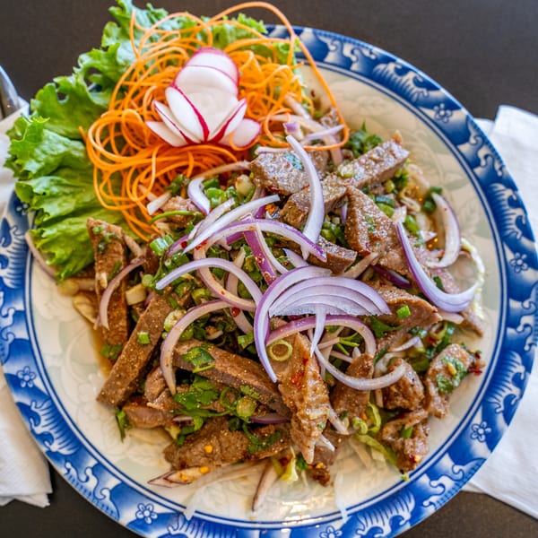 Thai beef salad with red onions, green herbs, and shredded carrots on a blue and white plate.