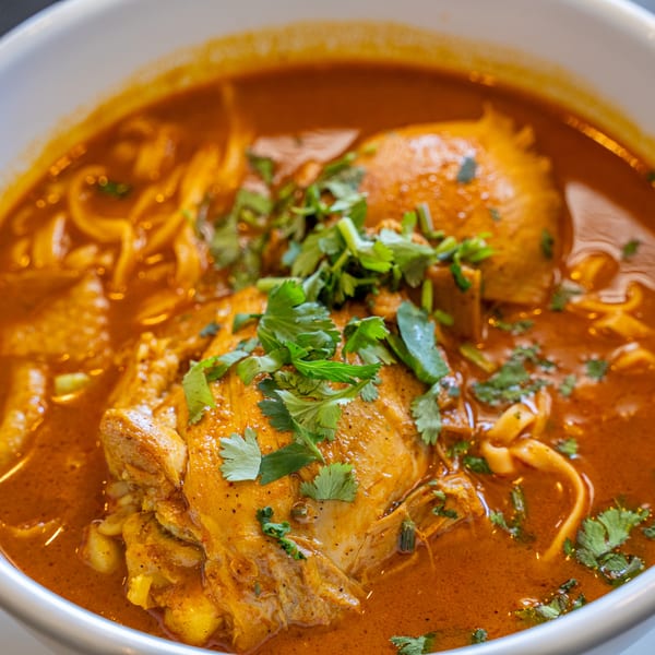 Close-up of a bowl of Thai Khao Soi with chicken, noodles, and cilantro in a rich red curry broth.