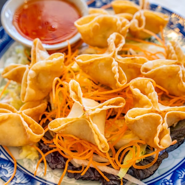 Crispy Thai crab rangoons with shredded carrots and lettuce, served with a side of sweet chili sauce.